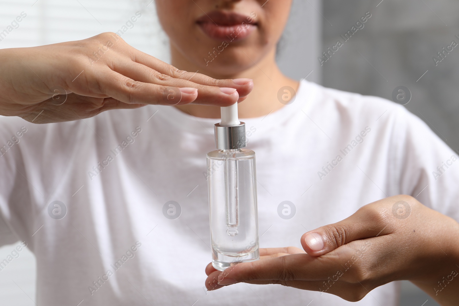 Photo of Woman with bottle of cosmetic serum on blurred background, closeup