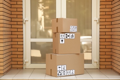 Photo of Cardboard boxes with different packaging symbols on floor near entrance. Parcel delivery
