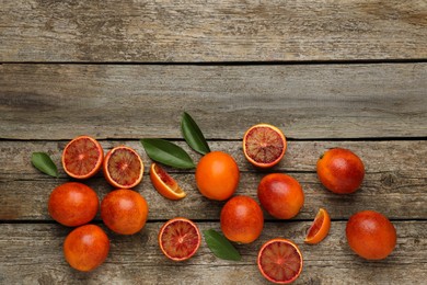 Photo of Many ripe sicilian oranges and leaves on wooden table, flat lay. Space for text