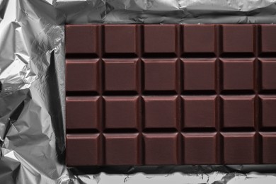 Photo of Delicious dark chocolate bar on foil, top view