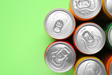 Energy drinks in wet cans on green background, top view. Space for text