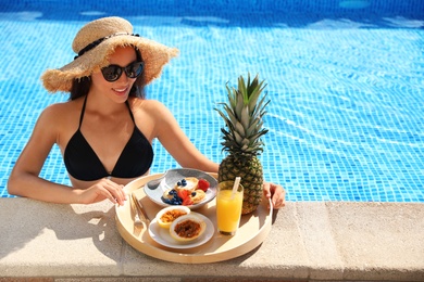 Young woman with delicious breakfast on tray in swimming pool. Space for text