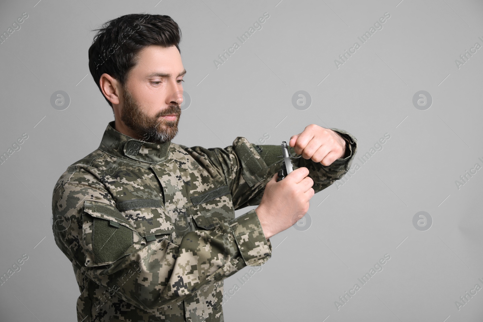 Photo of Soldier pulling safety pin out of hand grenade on light grey background. Military service