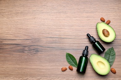 Photo of Bottles of essential oil, fresh avocado and almonds on wooden table, flat lay. Space for text