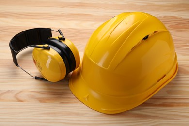 Photo of Safety equipment. Hard hat and protective headphones on wooden background, closeup