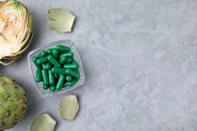 Photo of Bowl with pills and fresh artichokes on grey table, flat lay. Space for text
