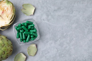 Bowl with pills and fresh artichokes on grey table, flat lay. Space for text