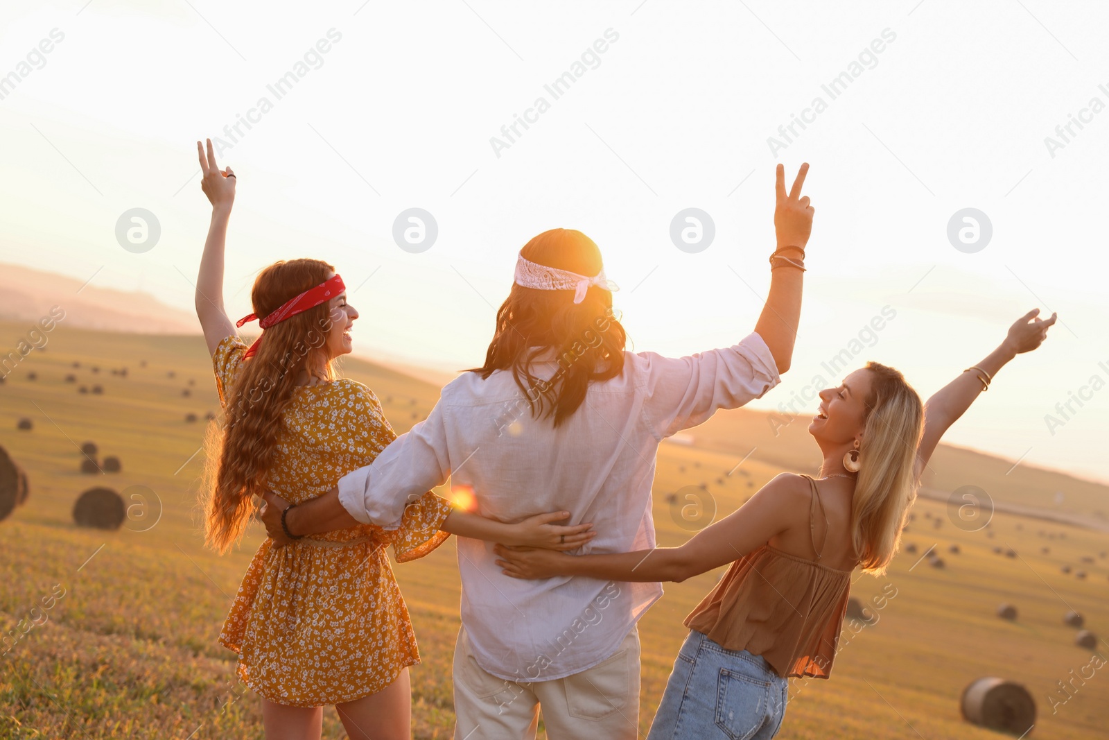 Photo of Happy hippie friends showing peace signs in field, back view