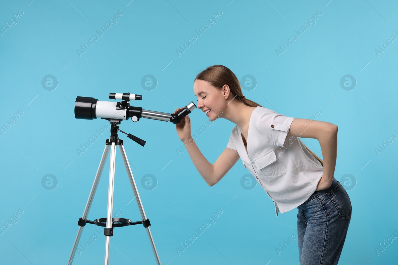 Photo of Young astronomer looking at stars through telescope on light blue background