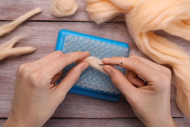 Woman felting from wool at wooden table, top view