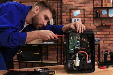 Repairman with screwdriver fixing coffee machine at table indoors