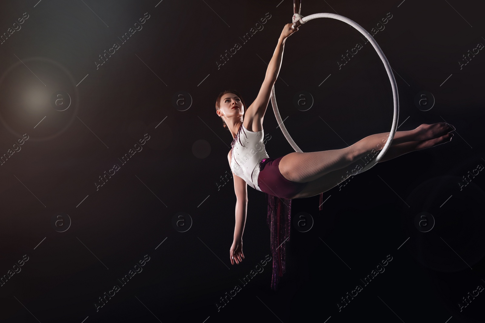 Photo of Young woman performing acrobatic element on aerial ring against dark background