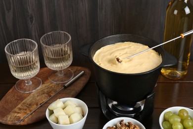 Photo of Fondue pot with tasty melted cheese, forks, wine and different snacks on wooden table