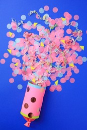 Photo of Colorful confetti and streamers bursting out of party cracker on blue background, flat lay