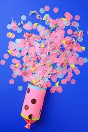 Colorful confetti and streamers bursting out of party cracker on blue background, flat lay