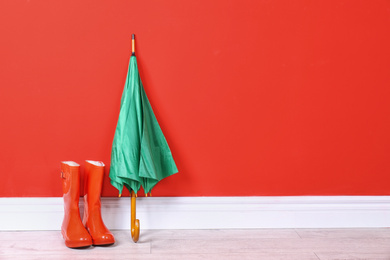 Photo of Beautiful green umbrella and rubber boots near red wall. Space for text