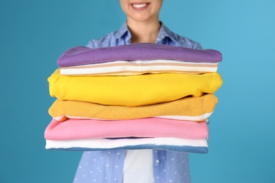 Photo of Young woman holding clean laundry on color background, closeup