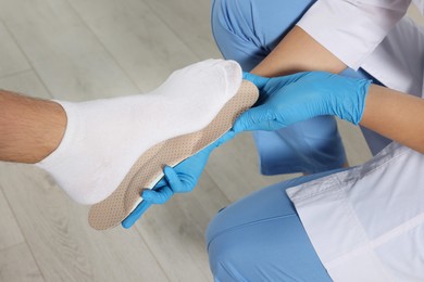 Orthopedist fitting insole to patient's foot in hospital, closeup