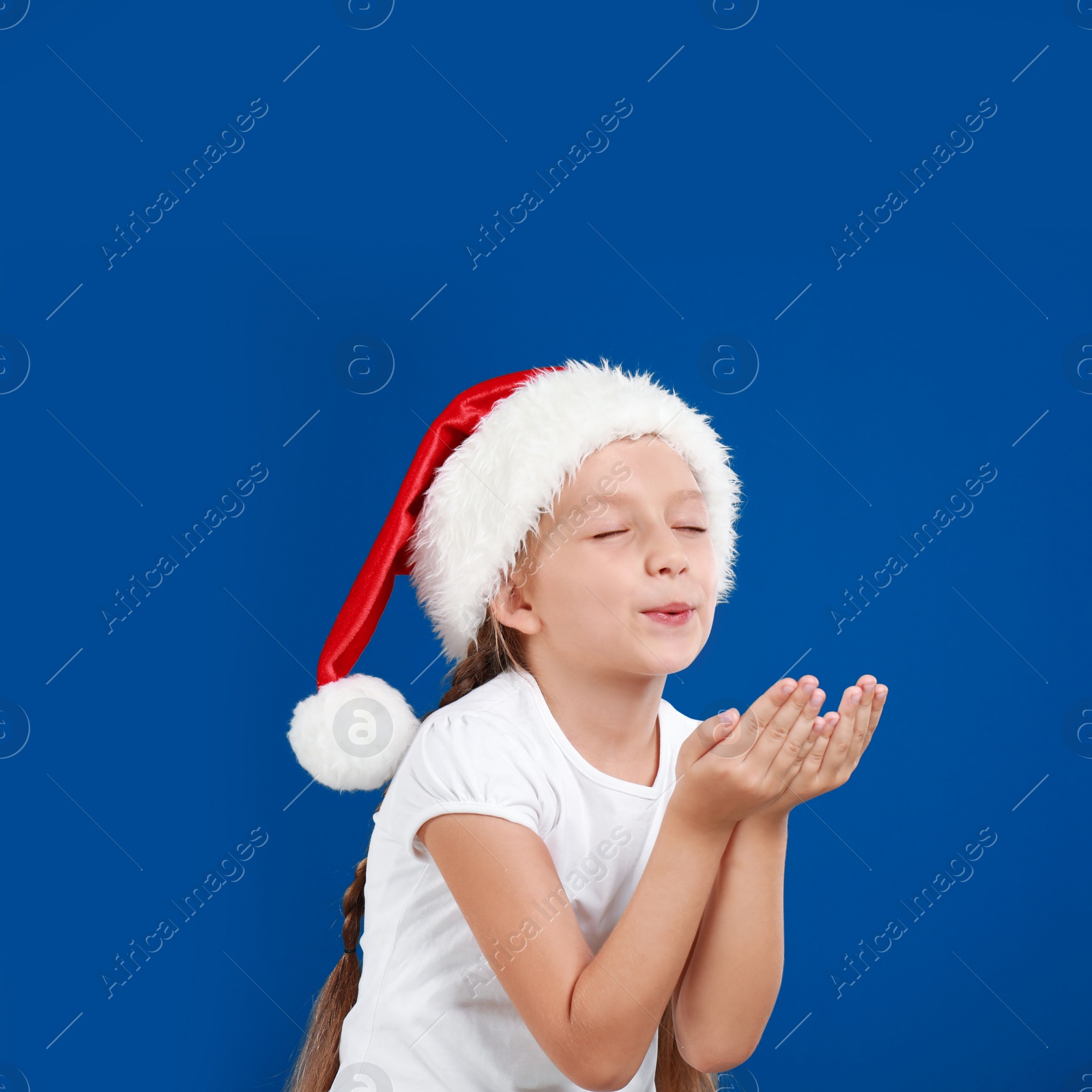 Image of Happy little child in Santa hat on blue background. Christmas celebration