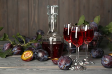 Photo of Delicious plum liquor and ripe fruits on grey wooden table, space for text. Homemade strong alcoholic beverage