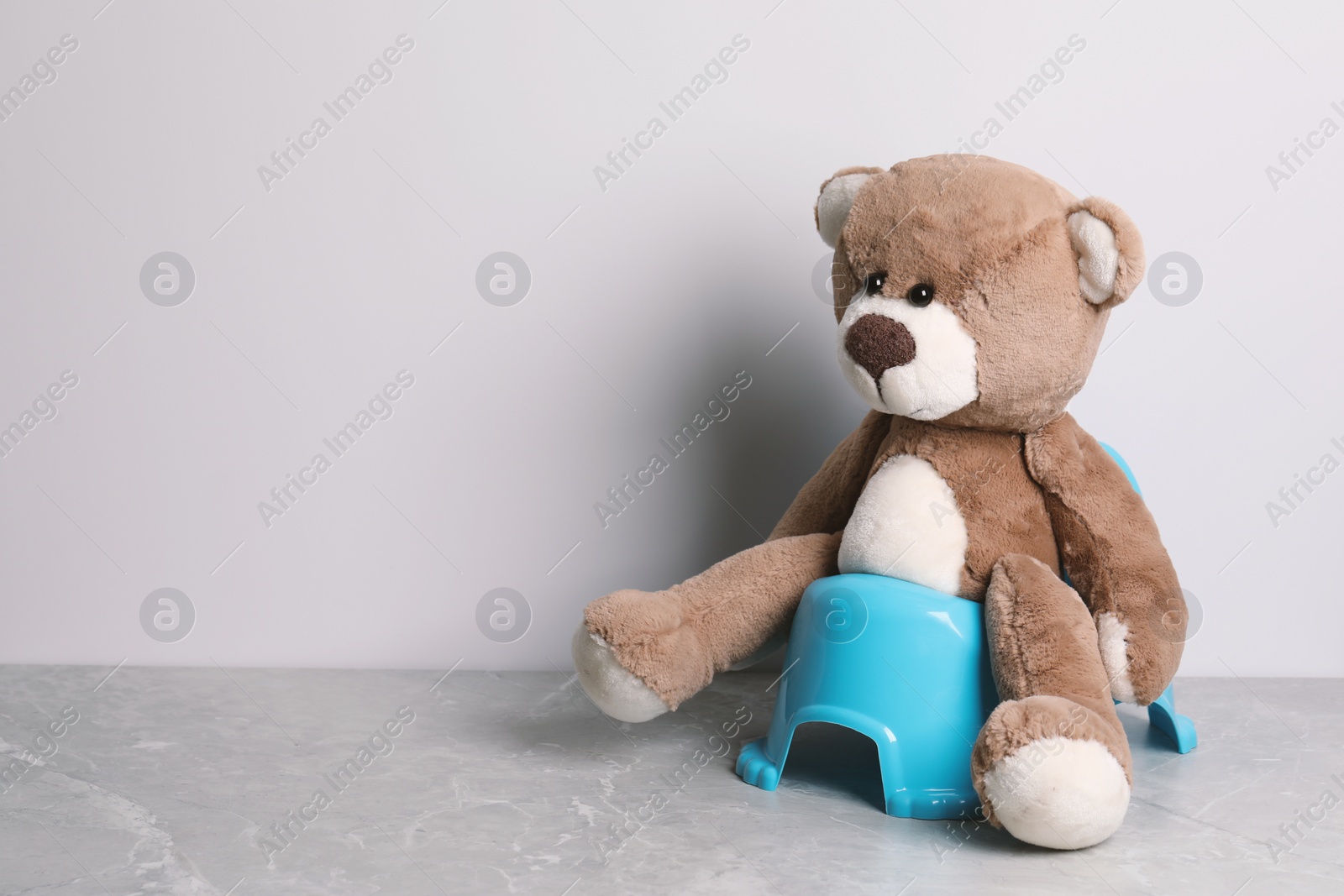 Photo of Teddy bear on baby potty near light wall, space for text. Toilet training