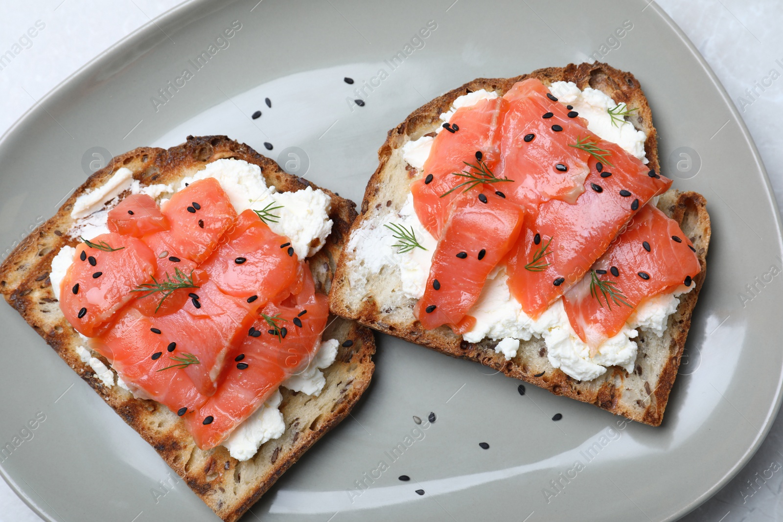 Photo of Delicious sandwiches with cream cheese, salmon and black sesame seeds on grey plate, top view