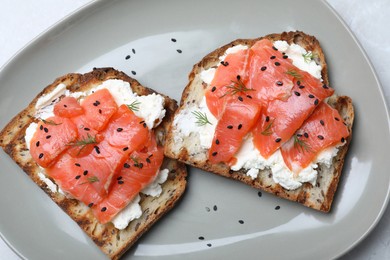 Delicious sandwiches with cream cheese, salmon and black sesame seeds on grey plate, top view