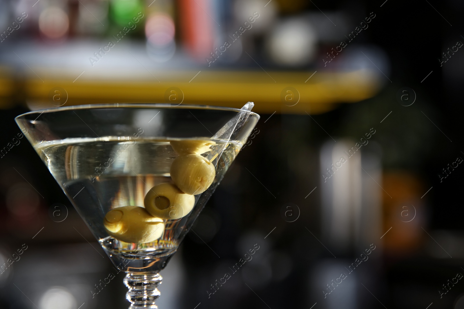 Photo of Glass of martini cocktail with olives in bar, closeup. Space for text