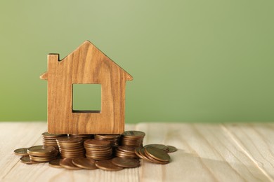 House model and coins on wooden table against green background, space for text