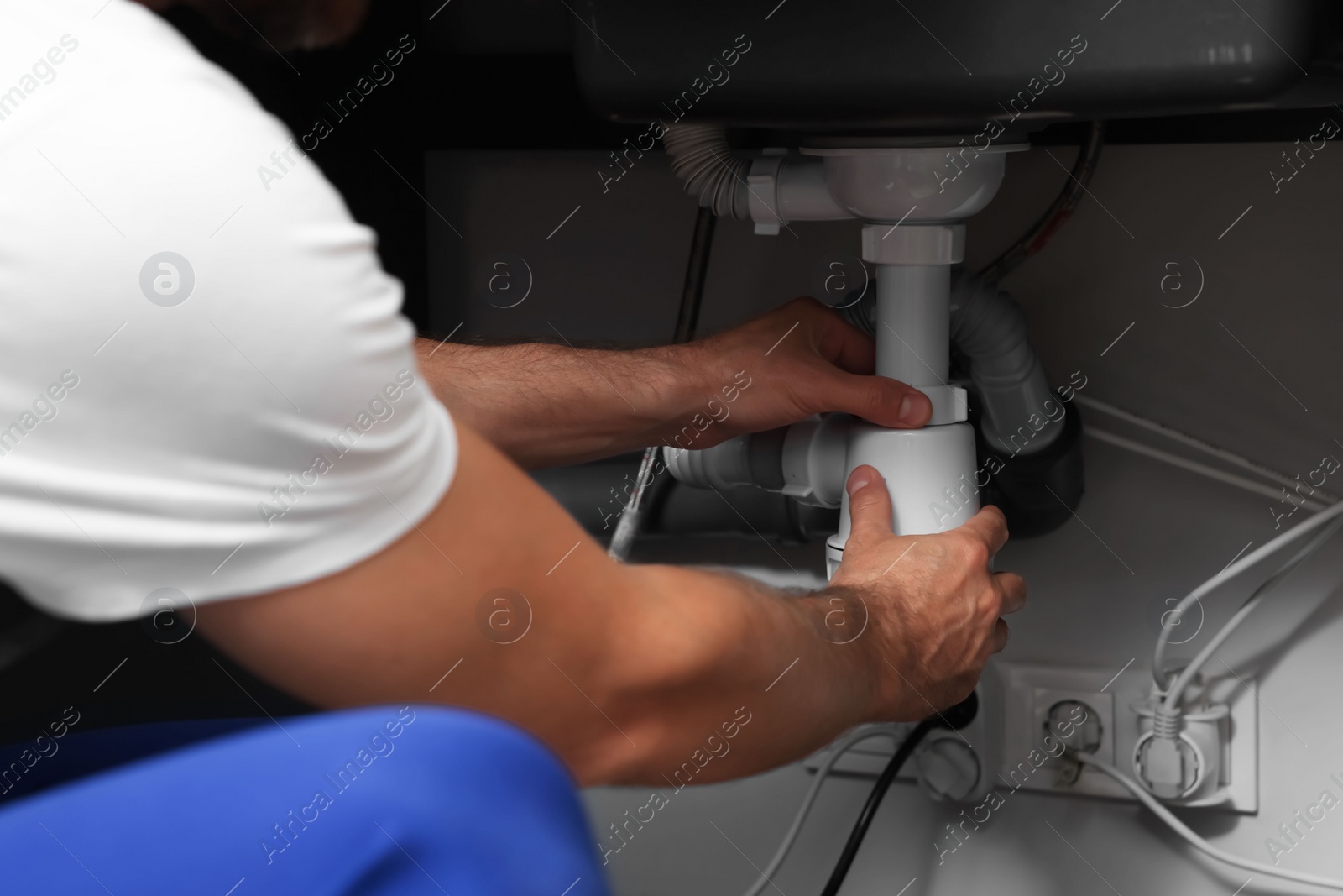 Photo of Professional plumber in uniform fixing sink, closeup