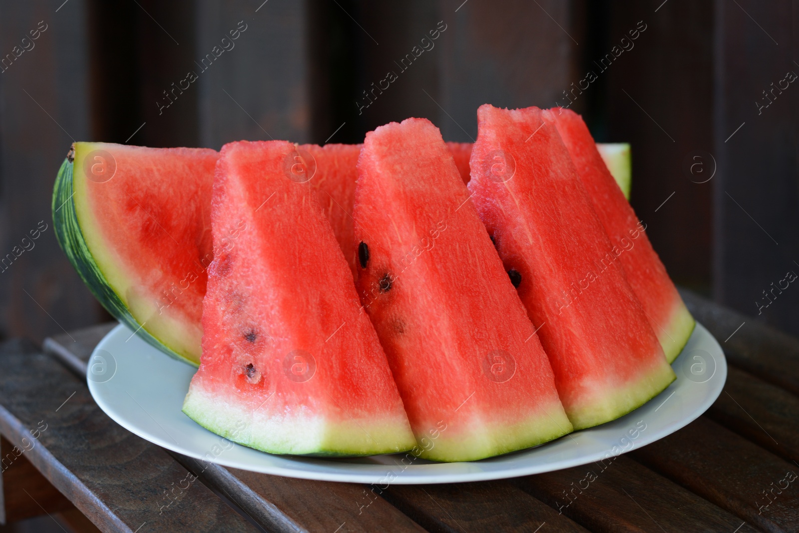 Photo of White plate with sliced watermelon on wooden stool outdoors