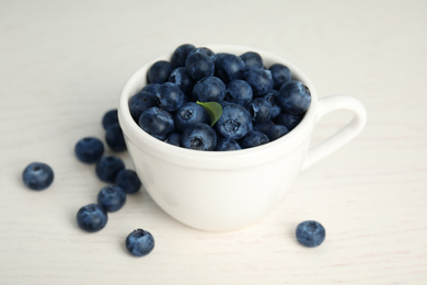 Photo of Fresh ripe blueberries in cup on white wooden table