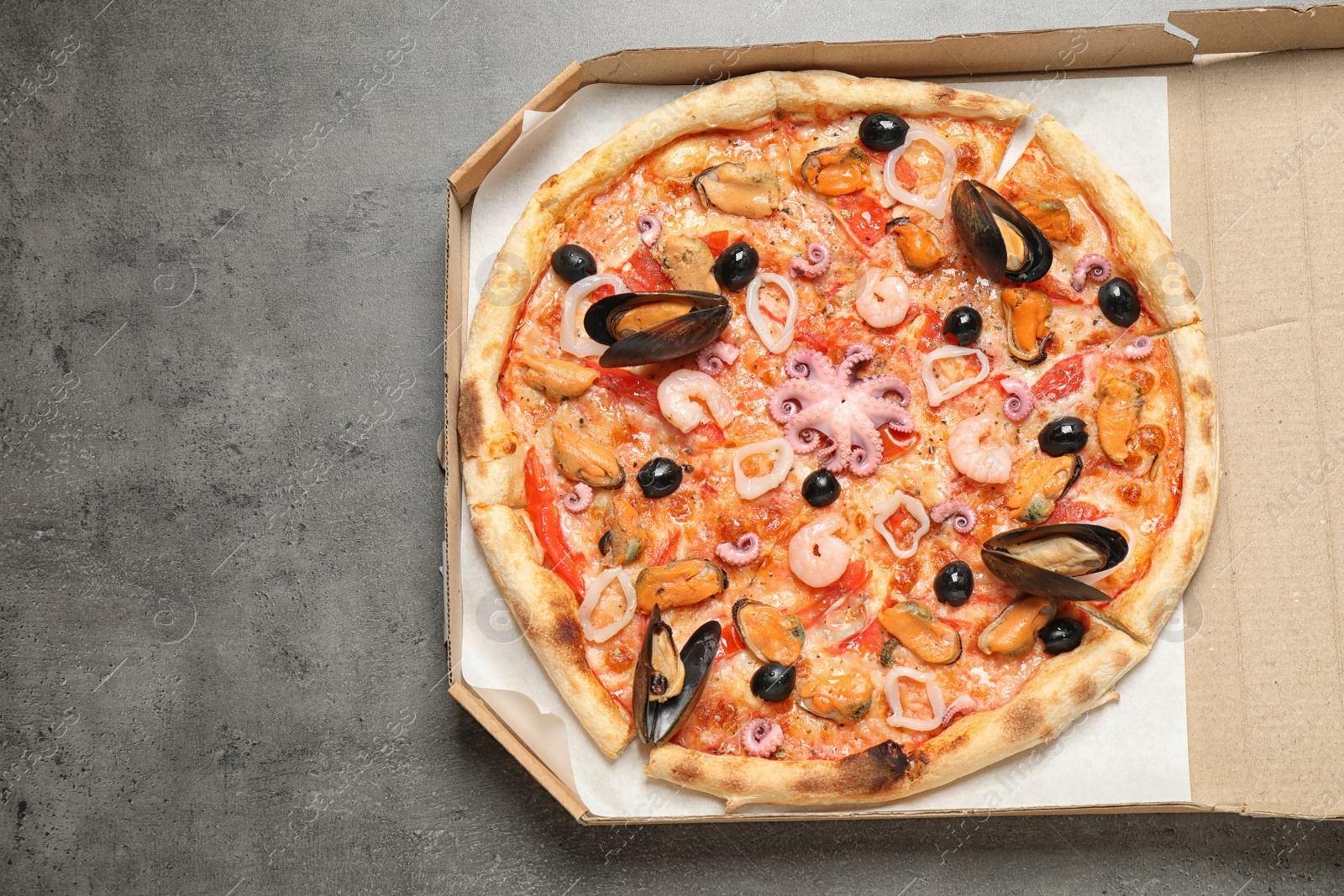 Photo of Delicious seafood pizza in box on grey table, top view