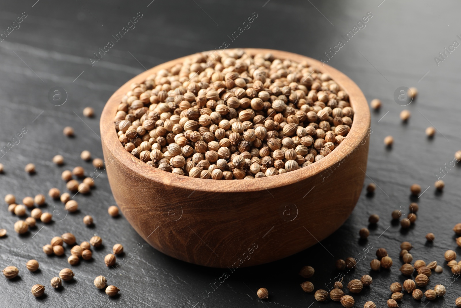 Photo of Dried coriander seeds in bowl on dark gray textured table, closeup