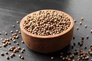 Dried coriander seeds in bowl on dark gray textured table, closeup