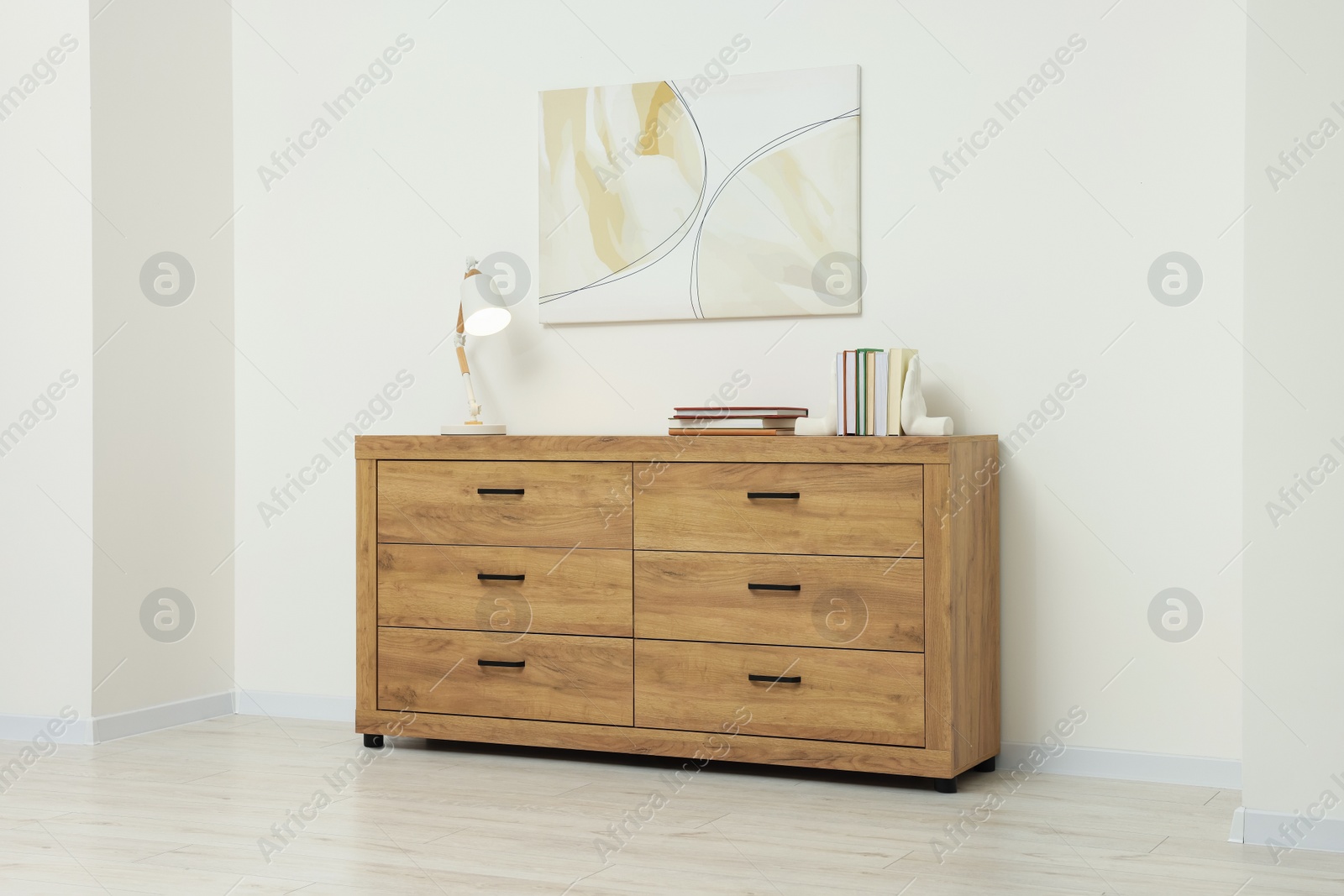 Photo of Wooden chest of drawers, lamp and beautiful picture on white wall indoors. Interior design