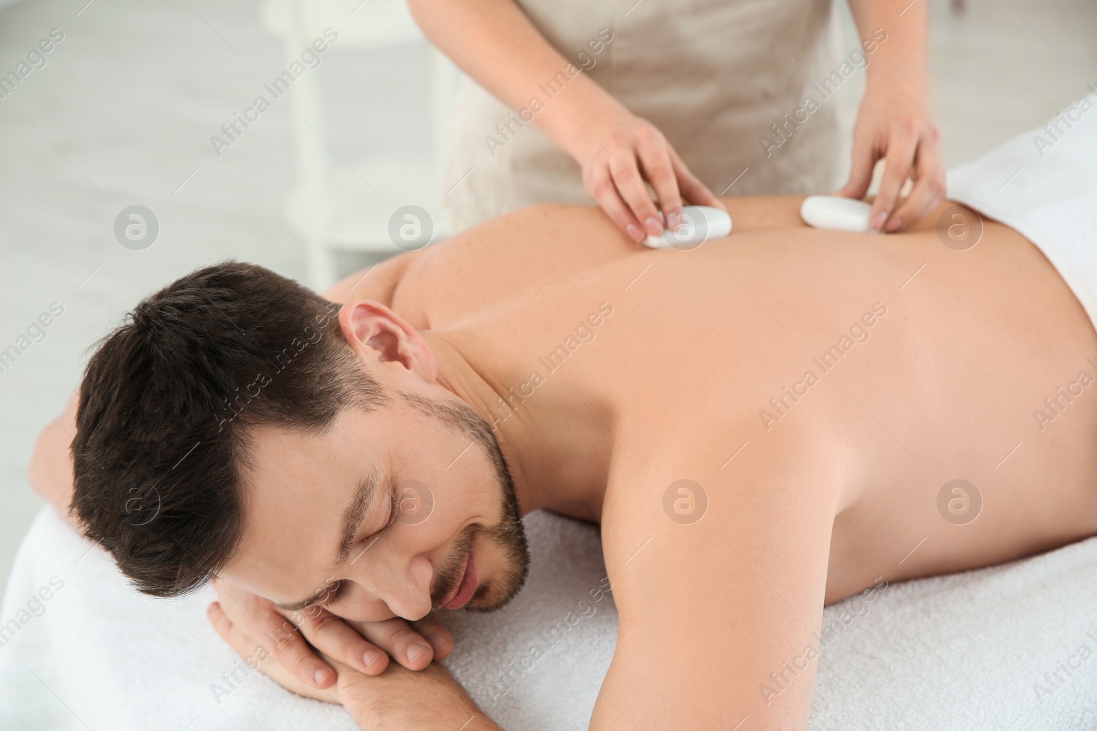 Photo of Handsome man receiving hot stone massage in spa salon