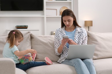 Photo of Little daughter playing while her mother working remotely on sofa at home