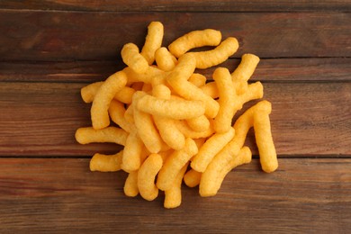 Photo of Heap of tasty cheesy corn puffs on wooden table, flat lay