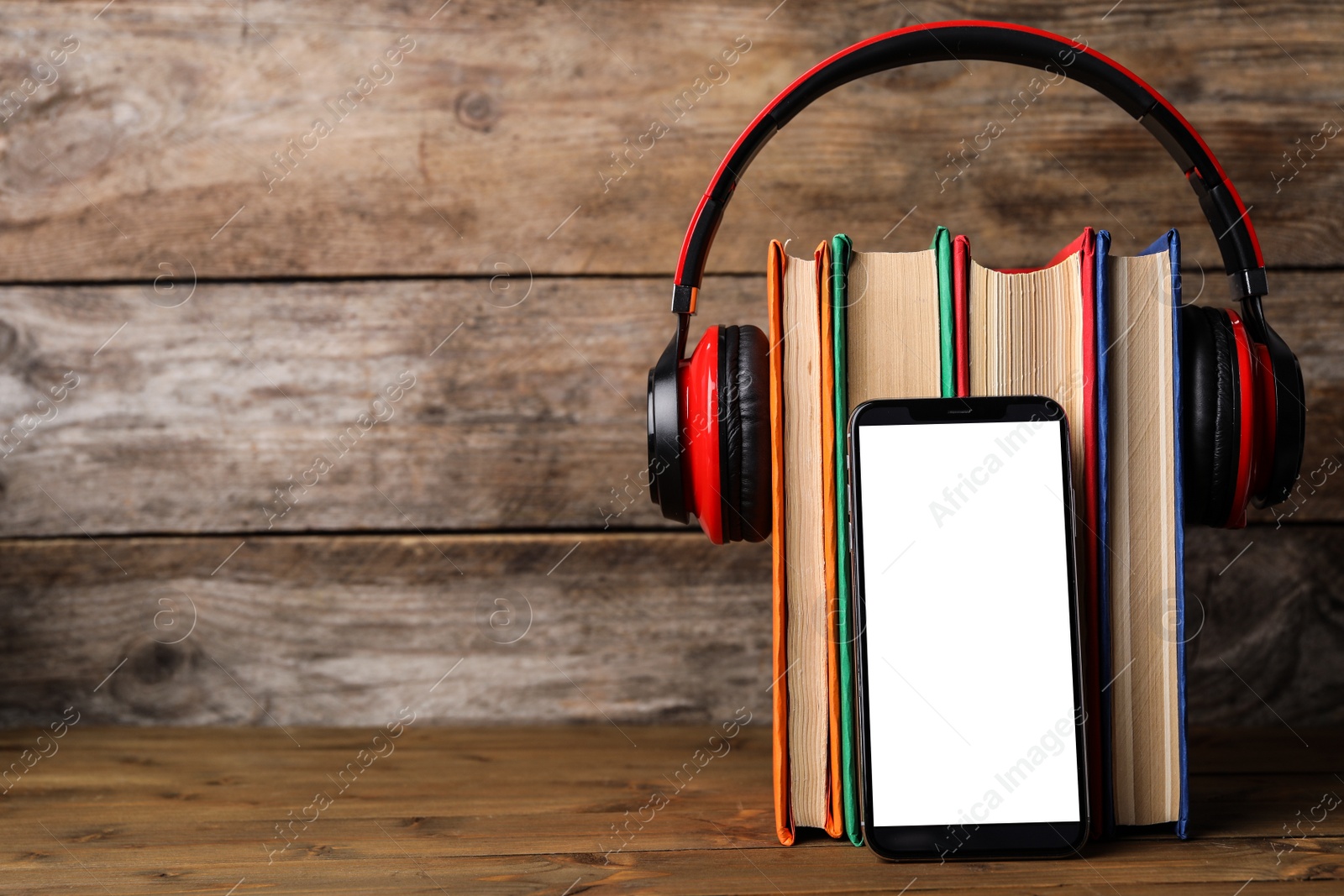 Photo of Books with modern headphones and smartphone on wooden table. Space for text