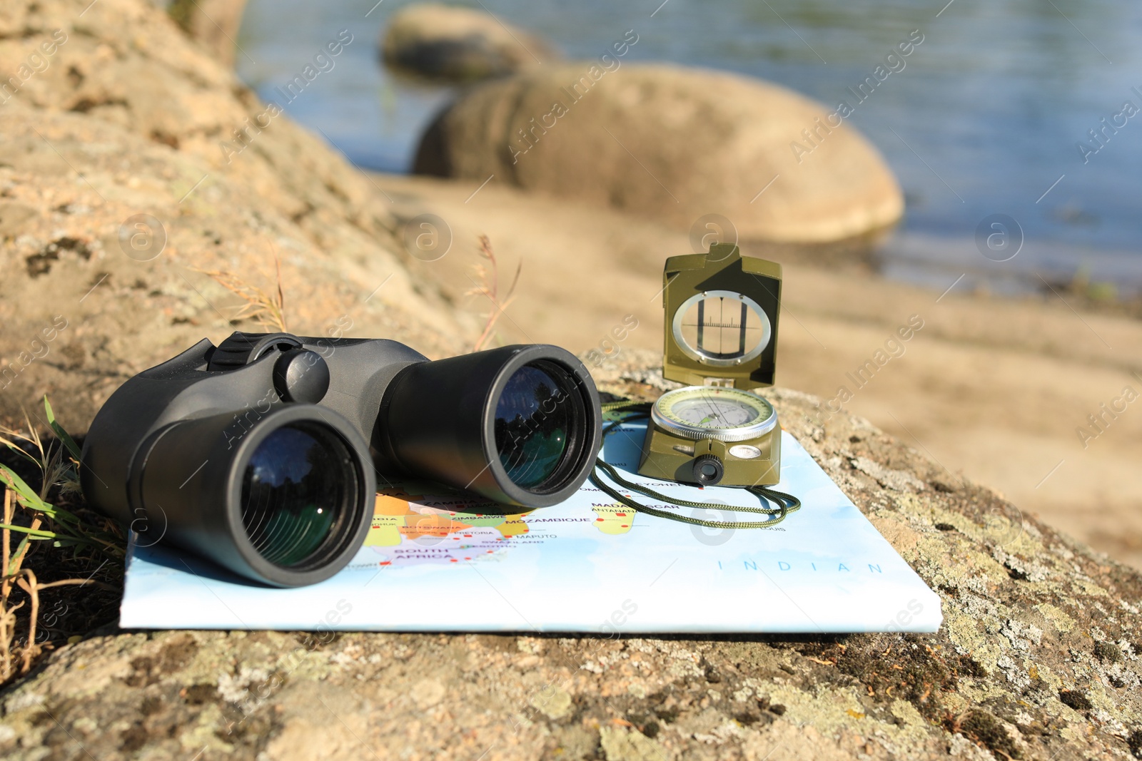 Photo of Binoculars, compass and map on stone near river, space for text. Camping equipment