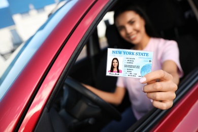 Happy young woman holding license while sitting in car, focus on hand. Driving school