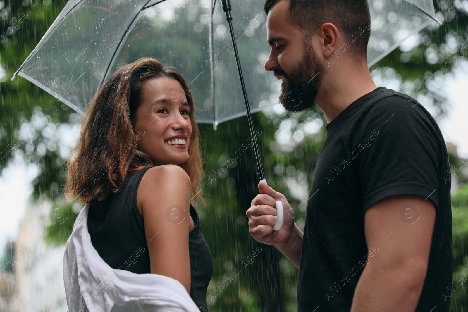 Photo of Young couple with umbrella enjoying time together under rain on city street