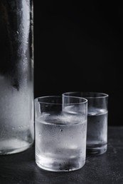 Photo of Vodka in shot glasses on table against black background, closeup