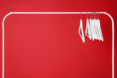 Photo of White clothes hangers on metal rack against red background. Space for text