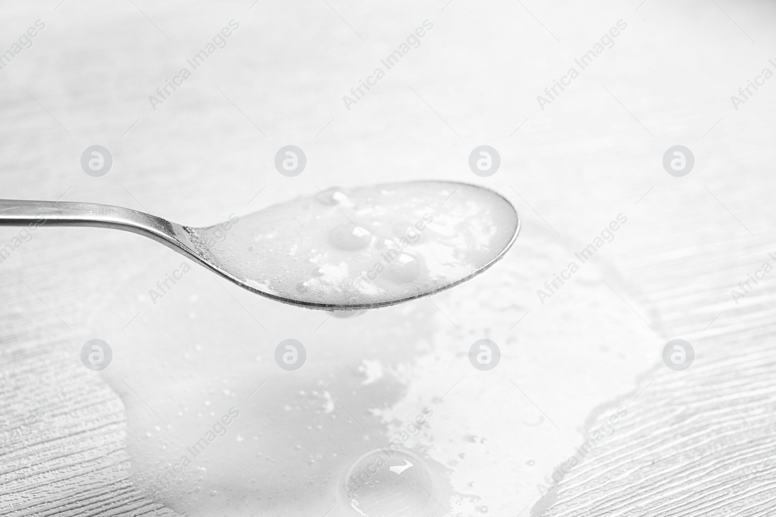 Photo of Chemical reaction of vinegar and baking soda in spoon over white wooden table