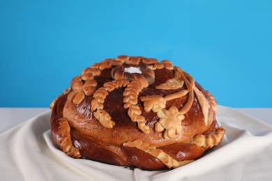 Photo of Korovai on tablecloth against light blue background. Ukrainian bread and salt welcoming tradition