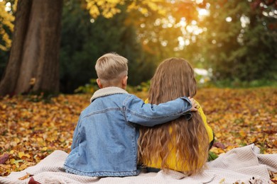 Photo of Children sitting on blanket in autumn park, back view