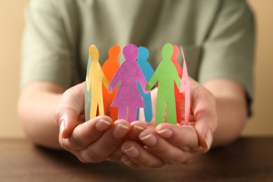Photo of Woman holding paper human figures at table, closeup. Diversity and inclusion concept