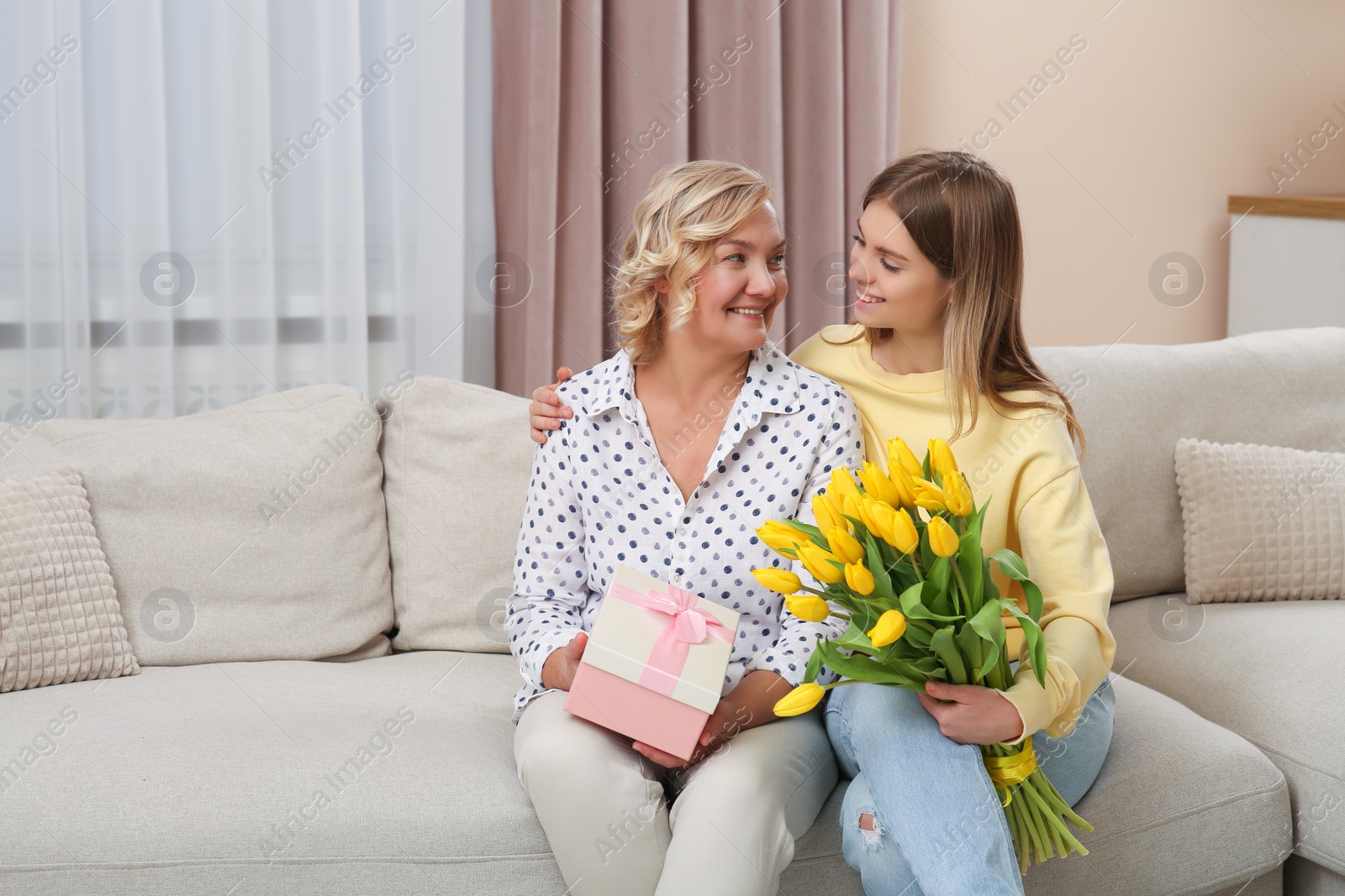 Photo of Young daughter congratulating her mom with flowers and gift at home. Happy Mother's Day